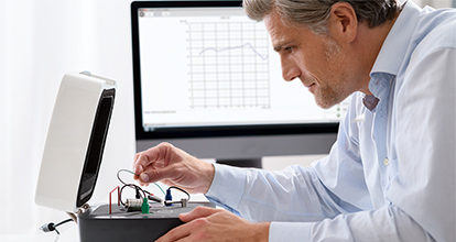 A man connects a hearing aid to the MedRx HIT box for testing. 